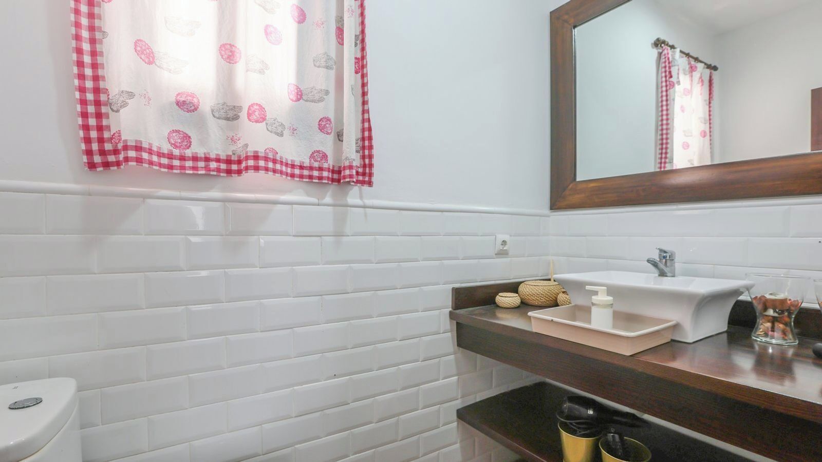 A bathroom with white tiled walls, a wooden countertop, a white sink, a mirror, and a toilet.