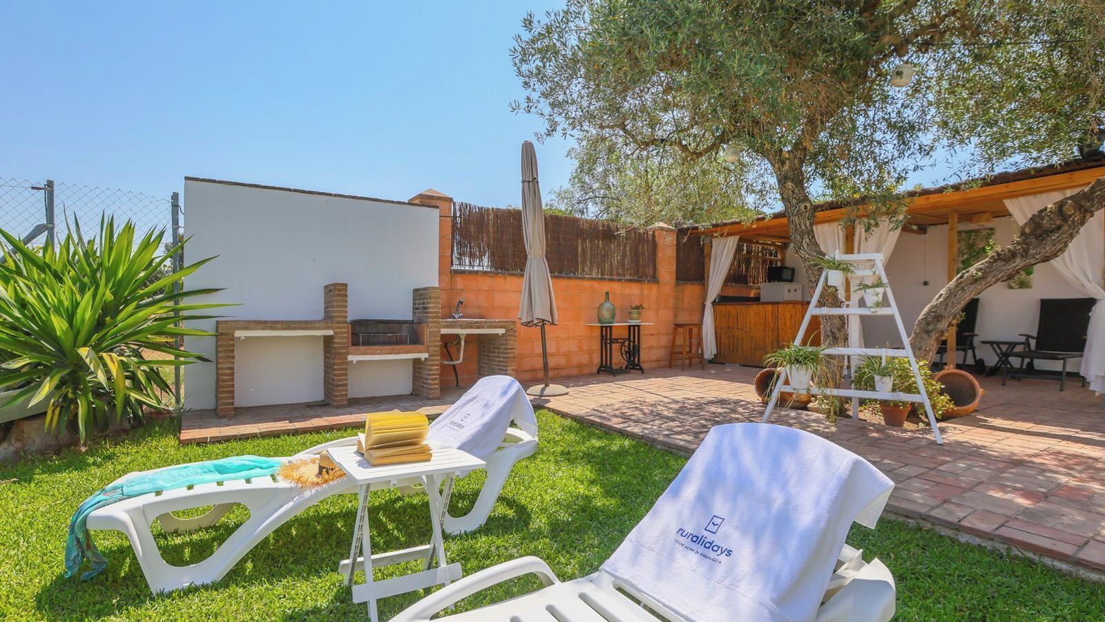 A patio with two lounge chairs, a barbecue grill, and a pergola with climbing plants.