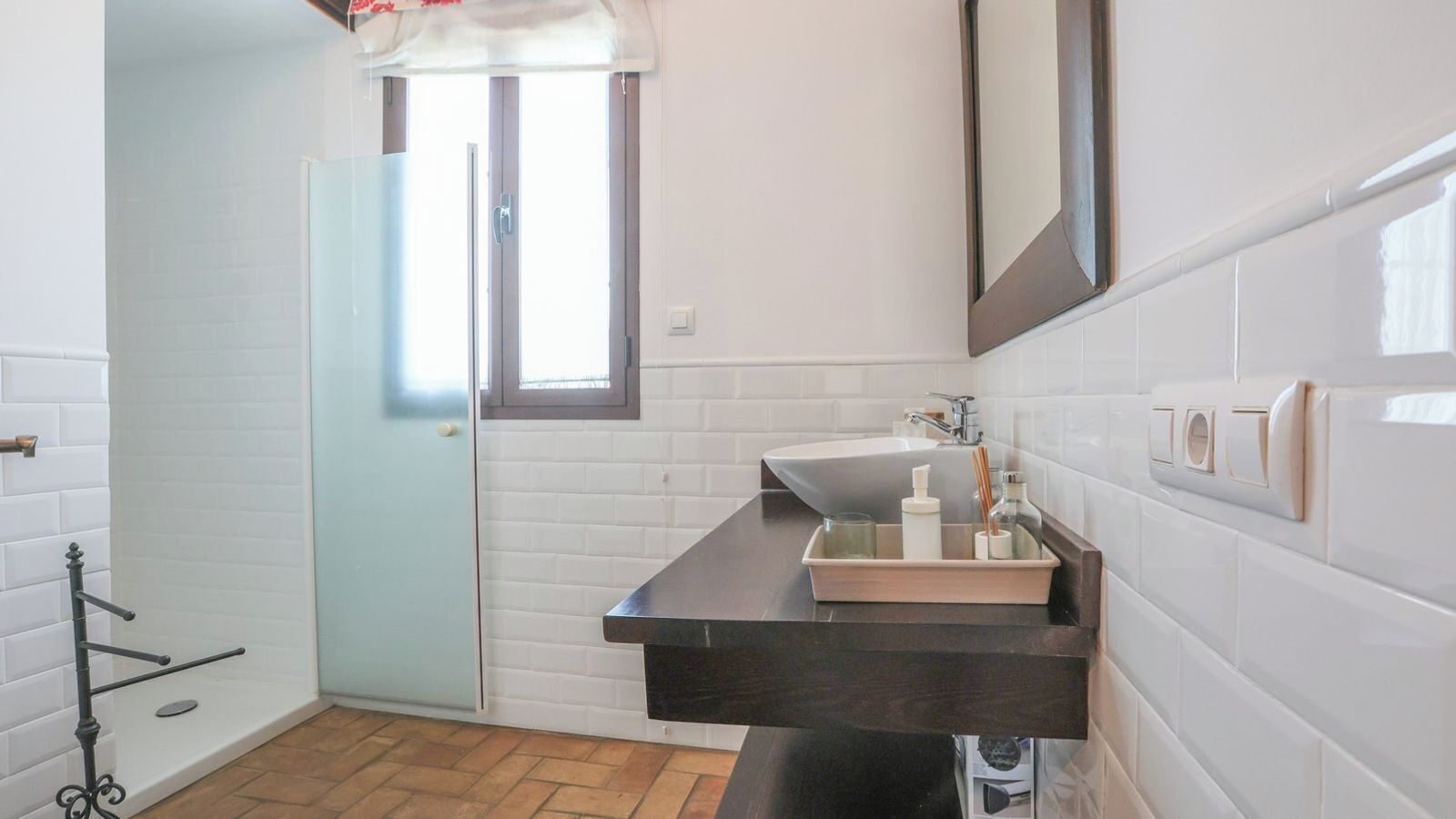 A bathroom with a white tiled wall, a sink with a mirror above it, and a window with a door.