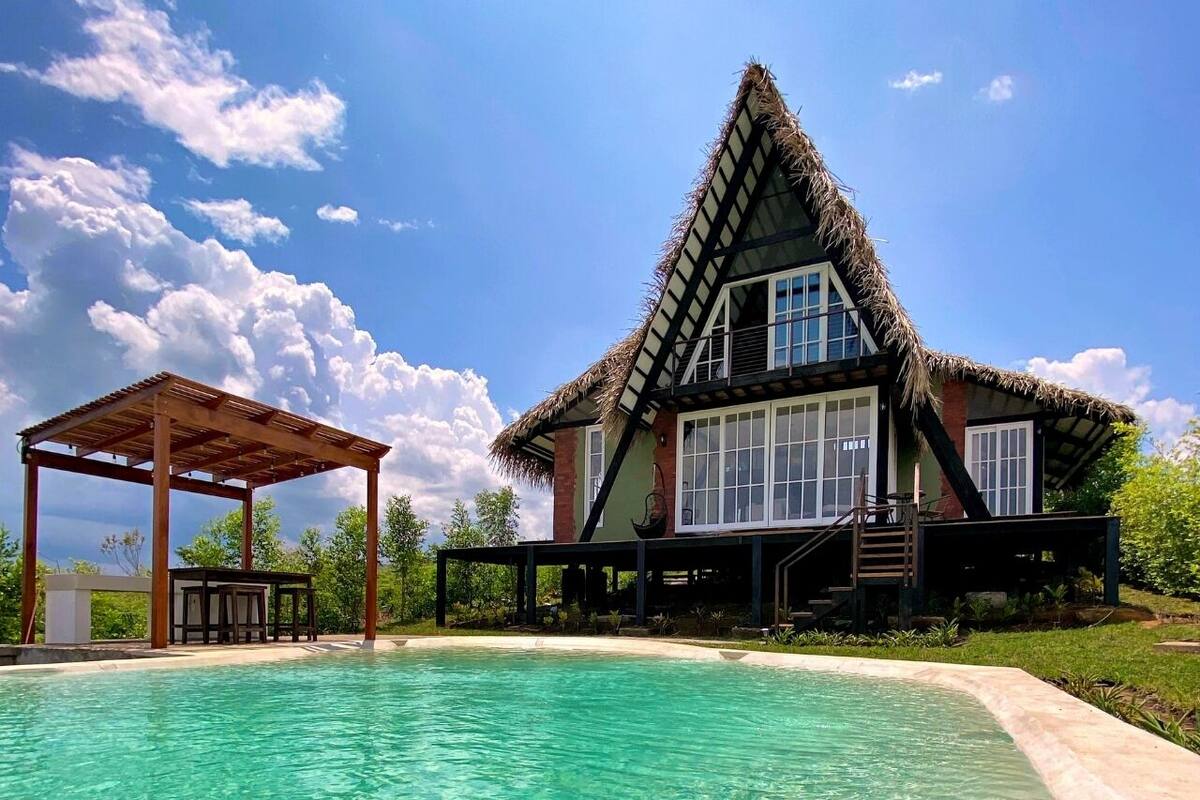 Una casa con techo de paja, piscina y zona exterior cubierta.