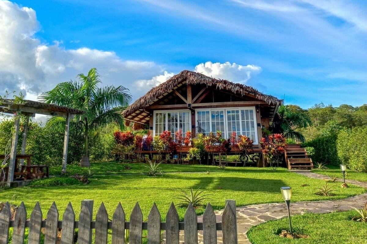 Una casa con techo de paja, rodeada de un jardín bien cuidado con diversas plantas y flores.