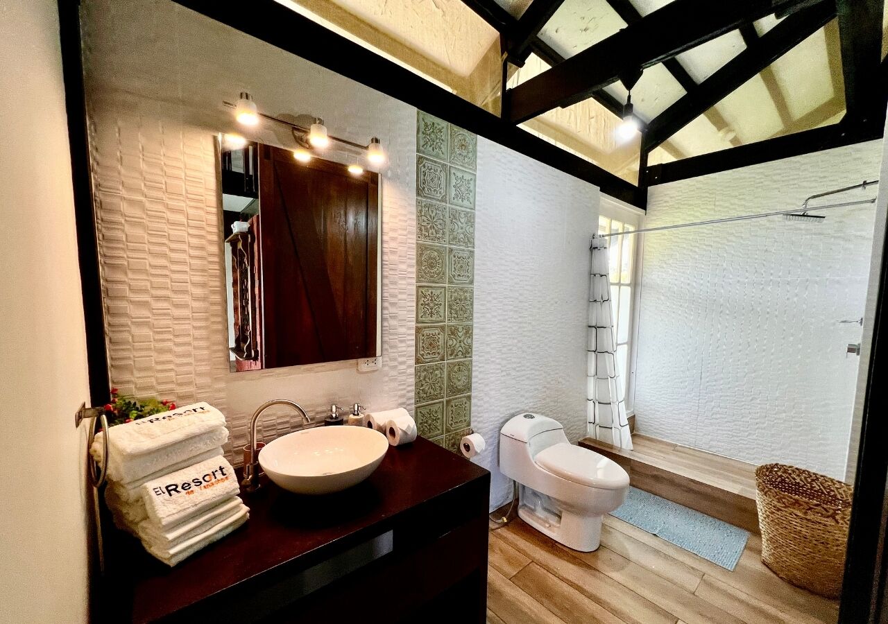 A modern bathroom with a large mirror, a round sink, and a toilet. There are towels stacked on the wall and a basket on the floor.