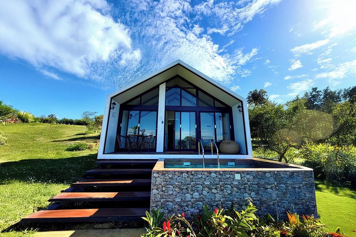 Una casa moderna con base de piedra, amplios ventanales de vidrio y un camino de piedra que lleva a la entrada.