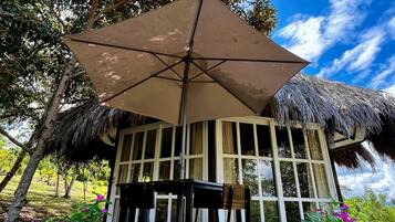 A thatched-roof structure with a large umbrella, a table, and chairs outside.