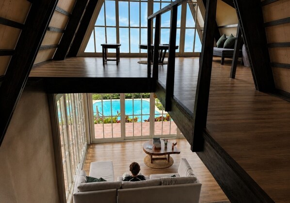 A high-ceilinged room with a view of a swimming pool, a sofa, and a coffee table. - El Resort de Yanashpa - Tarapoto (Cacatachi)
