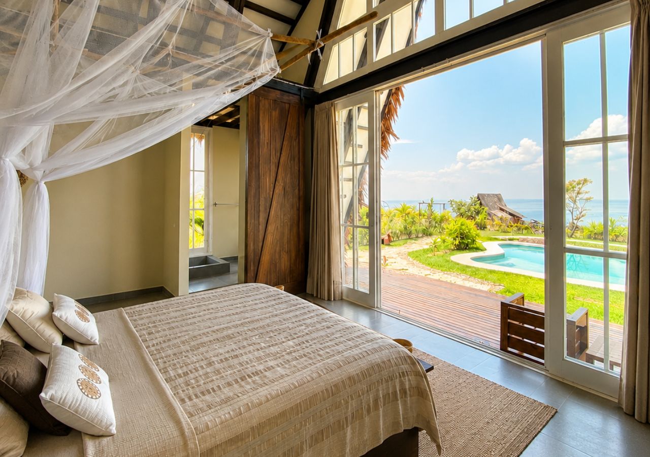 A bedroom with a large bed, a canopy, and a view of a swimming pool and landscape.
