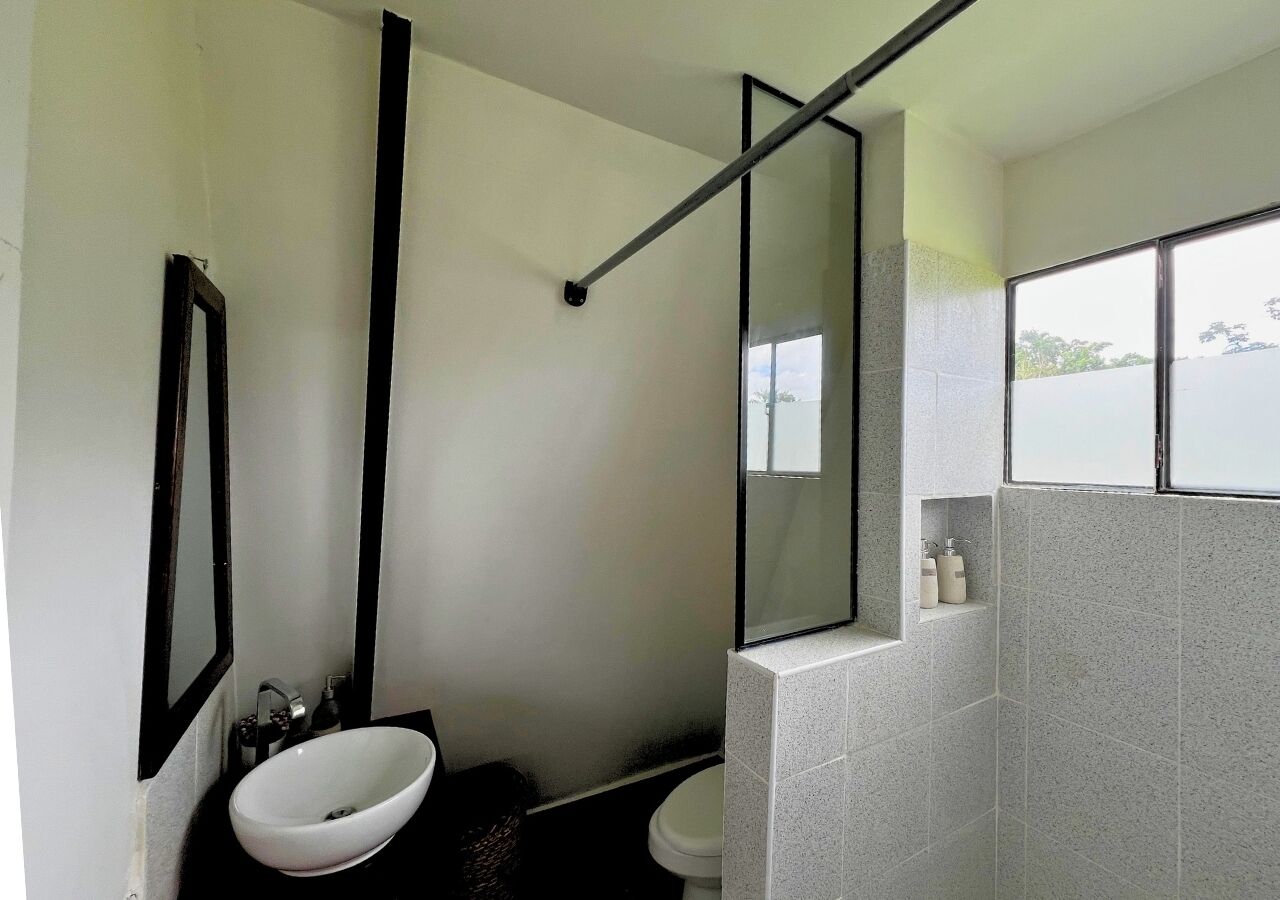 Une salle de bain moderne avec un lavabo blanc, un grand miroir et une fenêtre donnant sur l’extérieur.