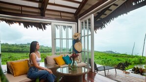 A woman sitting on a sofa with a glass table in a room with large windows and a view of a green landscape. - El Resort de Yanashpa - Tarapoto (Cacatachi)