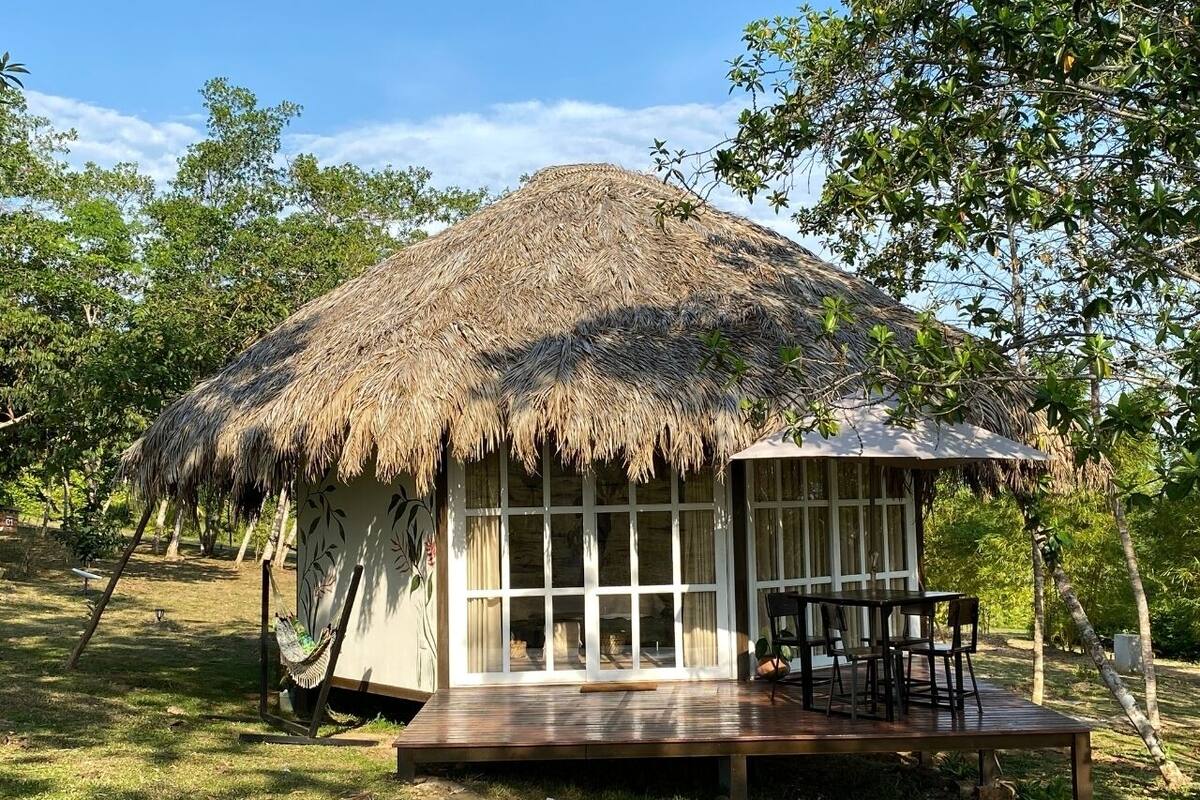 Una cabaña con techo de paja, un muelle de madera y una mesa con sillas.