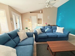 Ein Wohnzimmer mit zwei blauen Sofas, einem Holztisch und einem Deckenventilator.