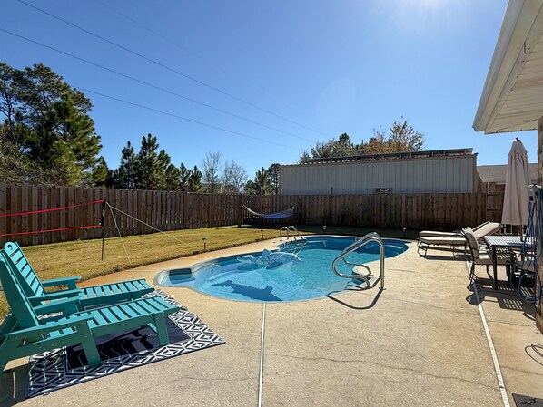 Ein Garten mit Pool, grünen Liegestühlen, einer Hängematte und einer überdachten Terrasse.