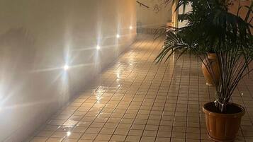 A corridor with tiled flooring, potted plants, and wall-mounted lights.