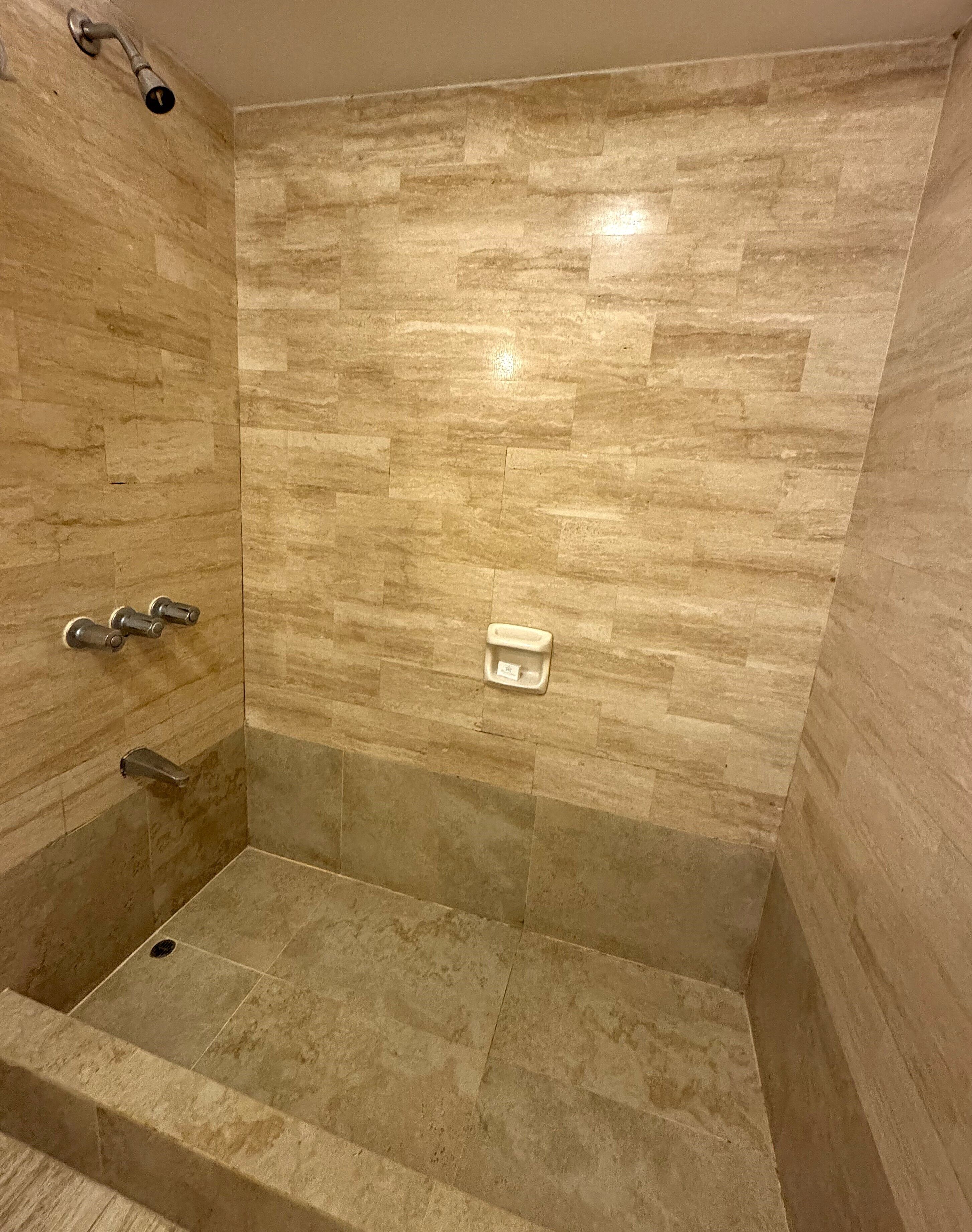 A shower with beige tiles and a handheld showerhead.