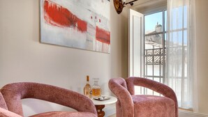 Ein Zimmer mit zwei rosafarbenen Sesseln, einem kleinen runden Tisch mit einer Flasche und Gläsern sowie einem großen, abstrakten Gemälde an der Wand.
