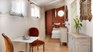Ein schmaler Flur mit Essbereich, der einen Marmortisch und Holzstühle umfasst. Ein Bett mit weißer Daunendecke sowie eine Kommode mit Spiegel sind ebenfalls zu sehen.