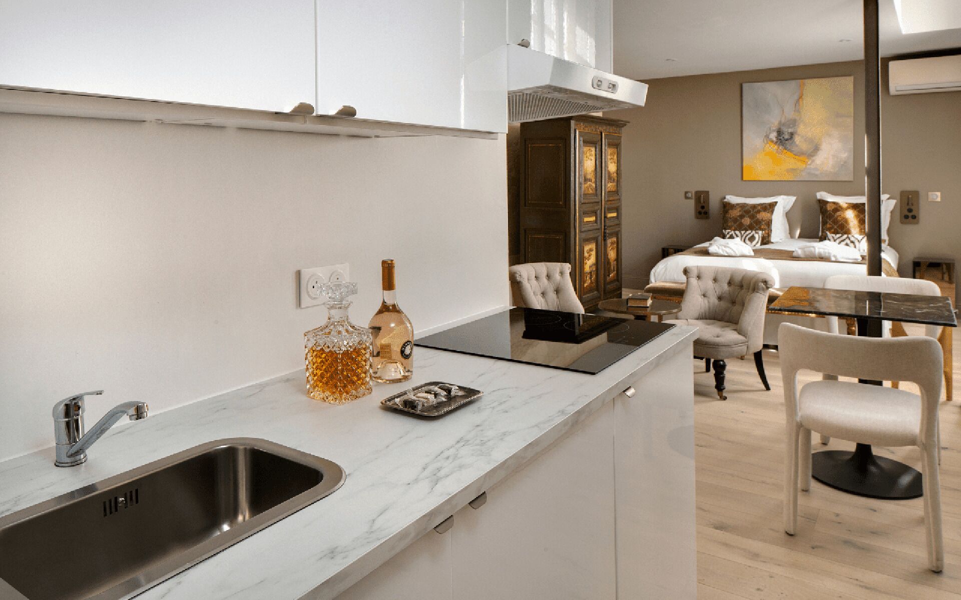 A modern kitchen with a built-in sink, a dining area with a table and chairs, and a bedroom with a bed and a painting.
