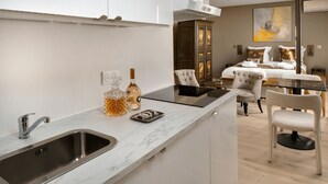 Een moderne keuken met een ingebouwd spoelbakje, een eethoek met een tafel en stoelen, en een slaapkamer met een bed en een schilderij.