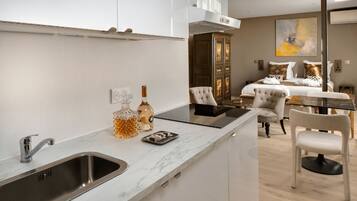 A modern kitchen with a built-in sink, a dining area with a table and chairs, and a bedroom with a bed and a painting.