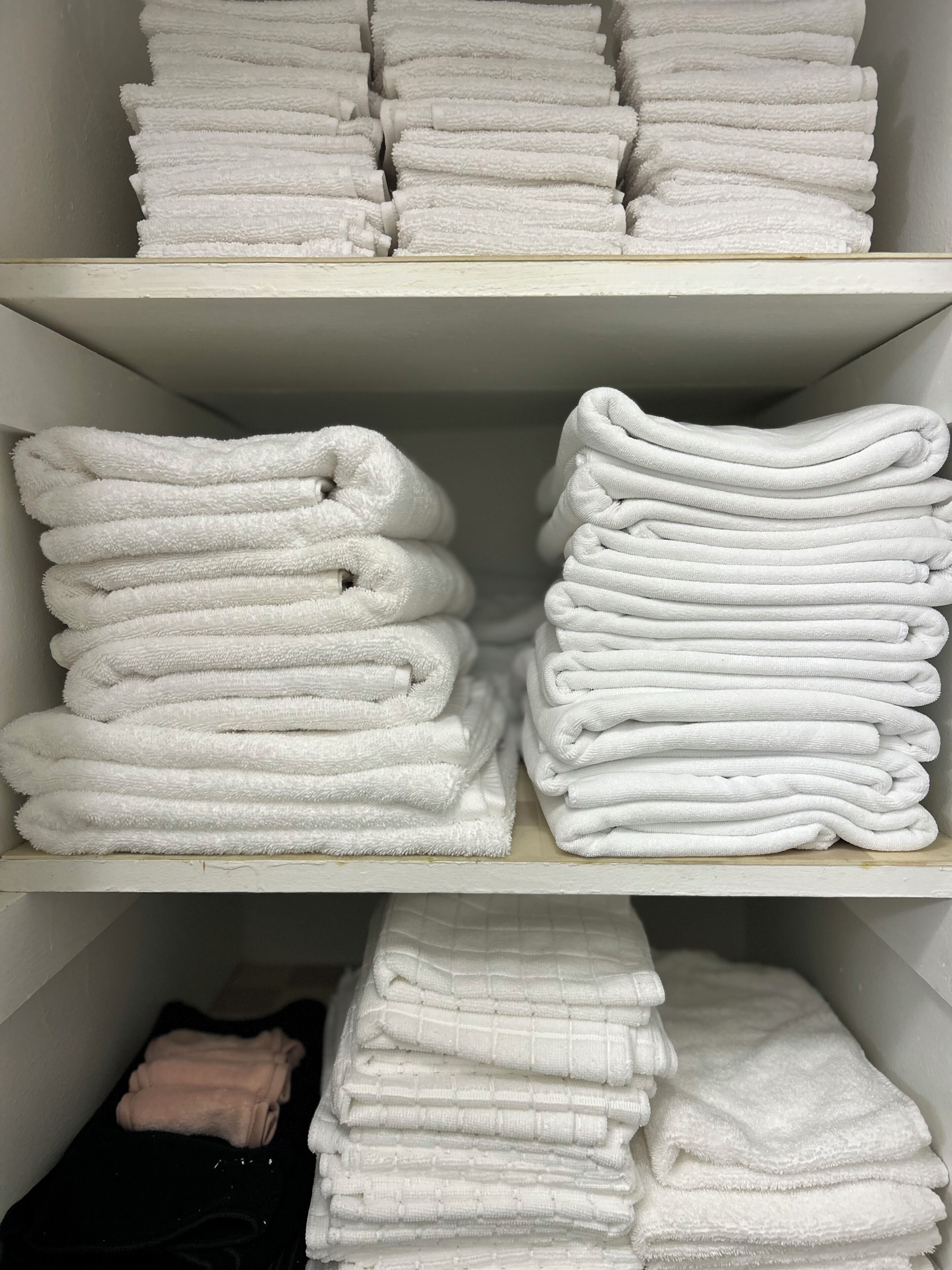 A storage area with neatly stacked white towels on shelves.