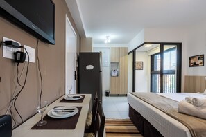 Una habitació d'hotel moderna amb zona de menjador, un llit amb edredó blanc i una televisió penjada a la paret.