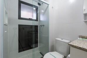 Un bany modern amb dutxa de vidre, vàter blanc i taulell de granat.