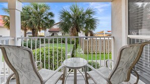 A balcony with two chairs and a small table, overlooking a garden with palm trees and a white fence. - No Worries, Relaxing Sound side Retreat with pool (Navarre)