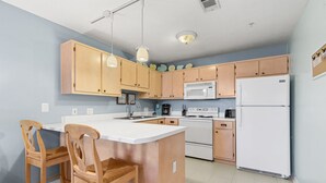 A kitchen with wooden cabinets, a white refrigerator, a microwave, a stove, and two wooden chairs. - No Worries, Relaxing Sound side Retreat with pool (Navarre)