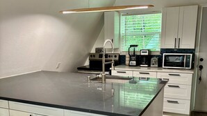 A modern kitchen with a large island, bar stools, white cabinetry, and a wooden ceiling. - Secluded Lake Retreat • Hot Tub, Fire Pit, Golf Cart + Mini Golf (Pottsboro)