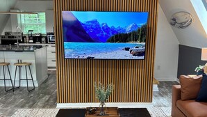 Moderni olohuone, jossa on suuri, seinälle asennettu litteänäyttöinen televisio, musta sohvapöytä, jossa on maljakko, ja ruskea nahkasohva.
