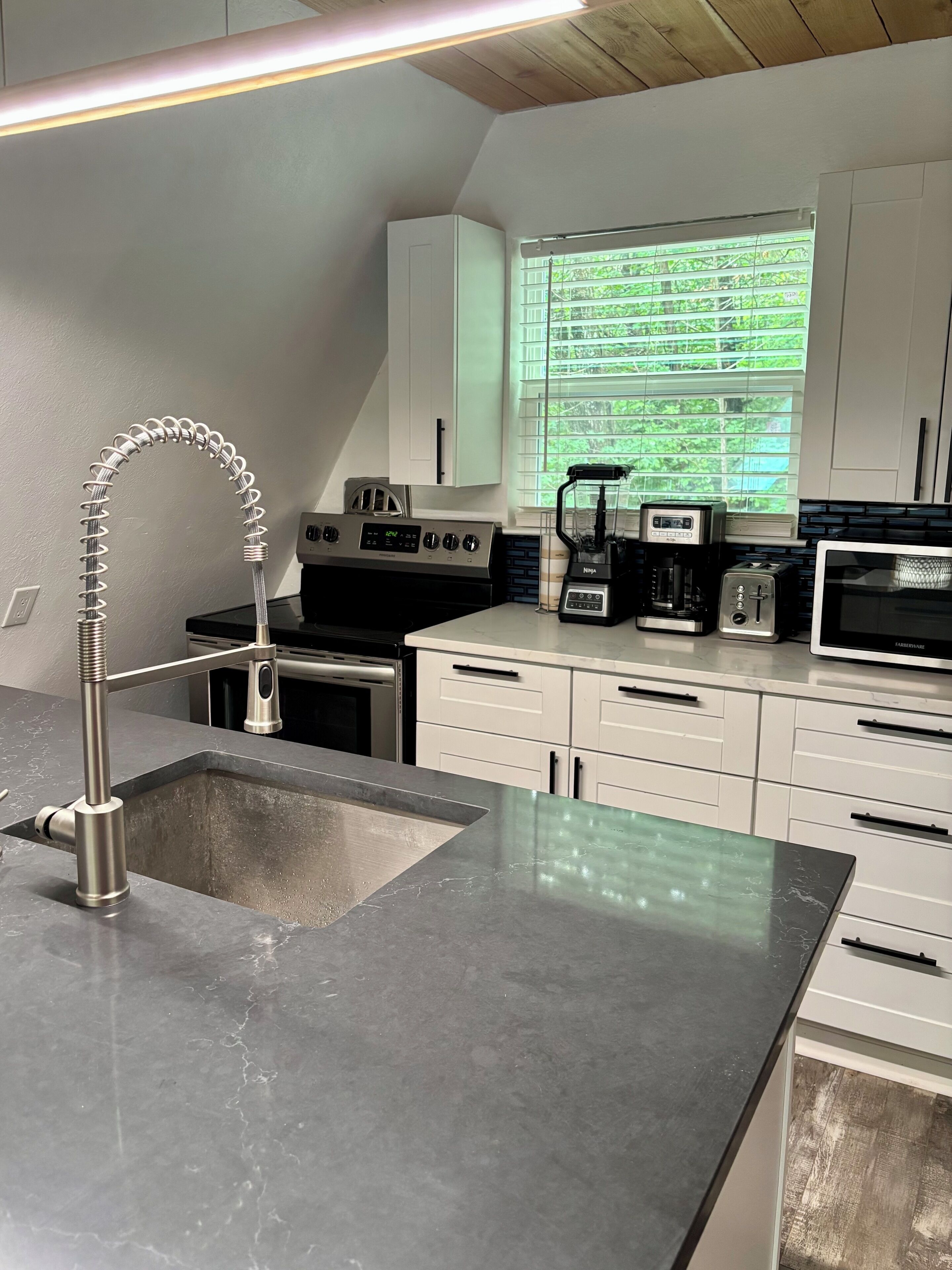 A modern kitchen with a stainless steel sink, a built-in stove, a coffee maker, and a microwave.