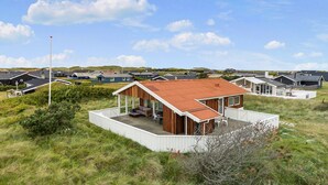 Een modern huis met een ruim terras, omgeven door een grasachtig landschap en andere huizen.