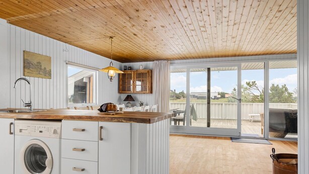 Een keuken met een houten plafond, een wasmachine, een eethoek met een tafel en stoelen, en een glazen schuifdeur die leidt naar een terras.