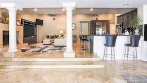 A spacious living area with a fireplace, a sofa, and a coffee table. There is a kitchen with a bar and stools.