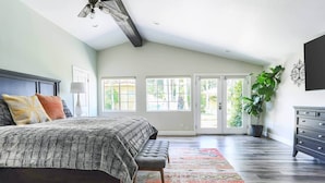 A bedroom with a large bed, a bench, a colorful rug, a potted plant, and a dresser.