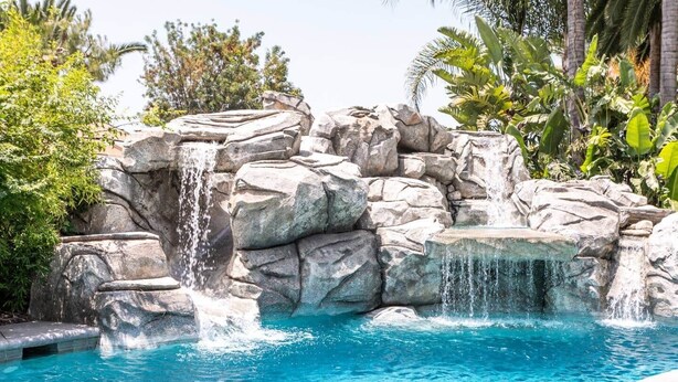 A pool with a waterfall feature surrounded by rocks and tropical plants.