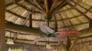 An outdoor kitchen with a stone countertop, a built-in grill, and a thatched roof structure.