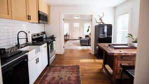A modern kitchen with wooden cabinets, a microwave, a stove, and a refrigerator. There is a rug on the floor and a plant in the corner. - Charming Oklahoma City Apartment in Central OKC (Oklahoma City)
