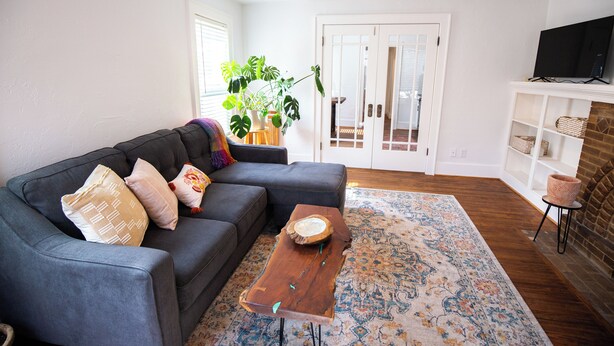 A living room with a gray sectional sofa, a wooden coffee table, a patterned rug, and a brick fireplace. - Charming Oklahoma City Apartment in Central OKC (Oklahoma City)