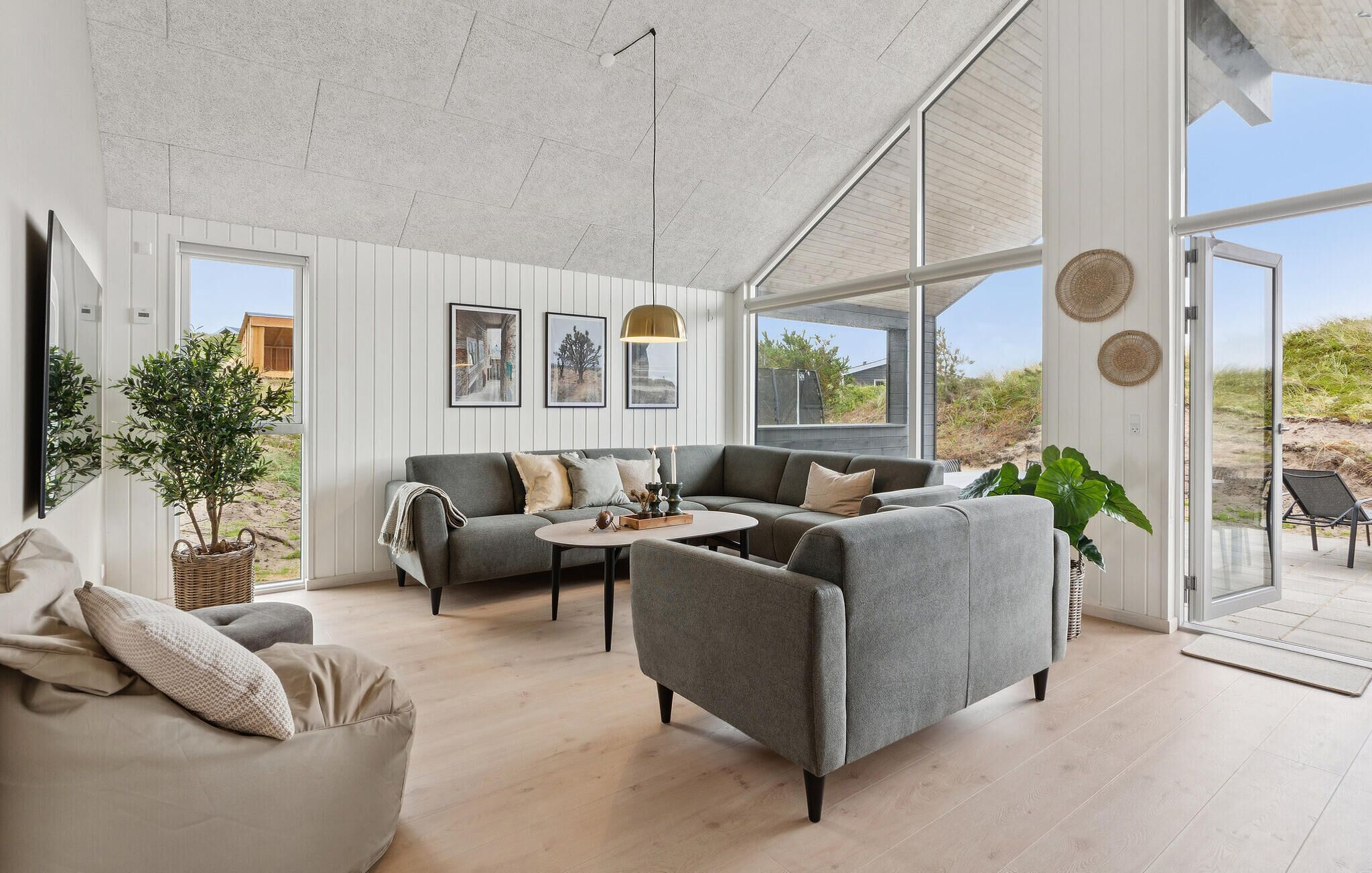 Ein modernes Wohnzimmer mit einem grauen Sofa, einem runden Couchtisch und einem großen Fenster mit Blick ins Freie.