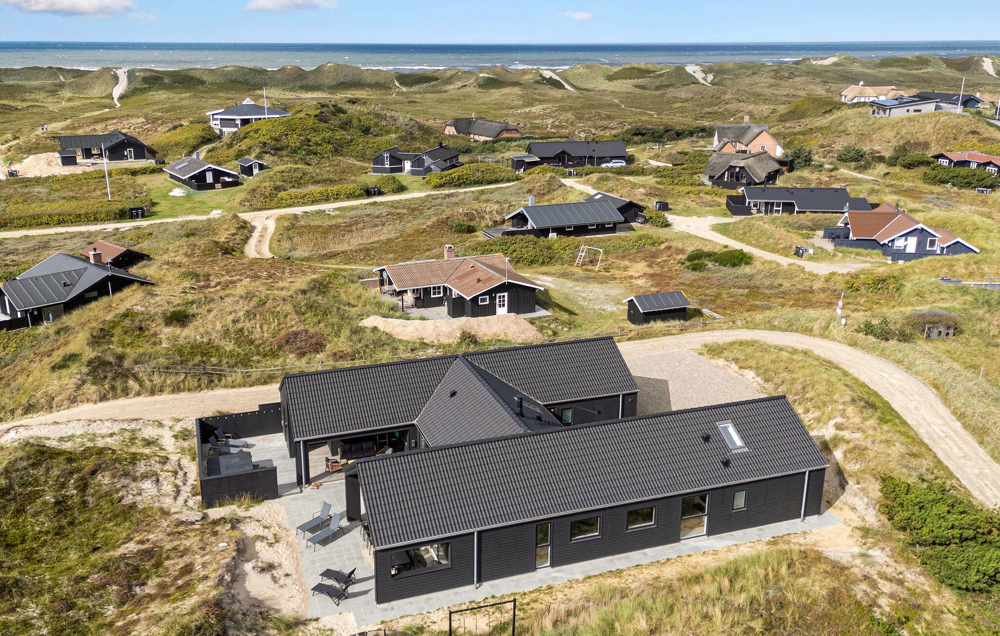 Ein Küstenwohngebiet mit mehreren Häusern, einige davon mit angebauten Garagen, und ein auffälliges Haus mit einer großen Terrassenfläche.