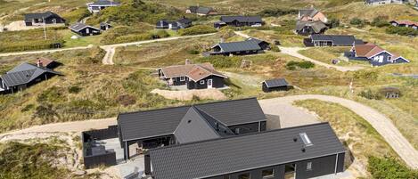 Ein Küstenwohngebiet mit mehreren Häusern, einige davon mit angebauten Garagen, und ein auffälliges Haus mit einer großen Terrassenfläche.