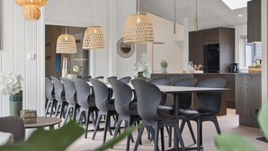 Un'area pranzo moderna con un tavolo lungo e diverse sedie, lampade a sospensione in vimini a soffitto e una cucina sullo sfondo.