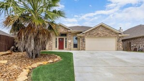 A two-story house with a stone facade, a red door, and a garage. - Aggie Escape  4BR+Fire Pit + Yard Games Near A&M (College Station)