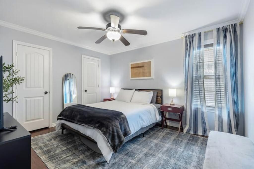 Quarto com cama, escrivaninha, cadeira, ventoinha no teto e cortinas.