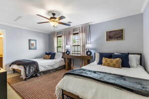 Ein Schlafzimmer mit zwei Betten, einem Deckenventilator, einem Schreibtisch mit Lampen und einem gerahmten Bild an der Wand.