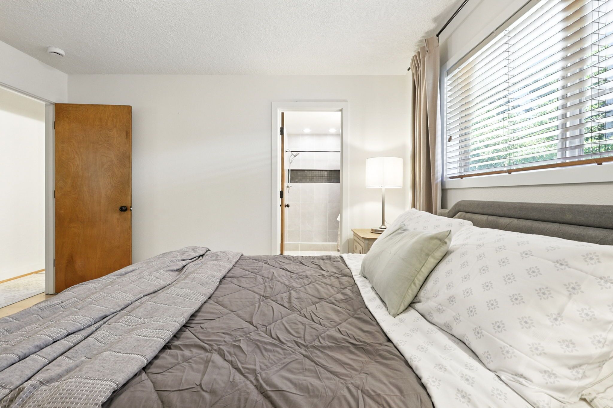 Un dormitorio con cama, mesita de noche, lámpara y ventana con persianas.
