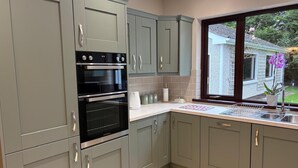 Eine moderne Küche mit grauen Schränken, einem Kombi-Backofen und einem Fenster mit Blick auf ein Haus und einen Garten.