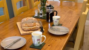 Ein Holztisch mit einer floralen Tischdekoration, einer Kaffeekanne, einer Brottafel und einer Kaffeetasse.