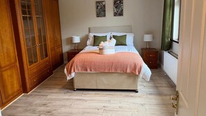 Ein Schlafzimmer mit einem großen Bett, einem Holzschrank, zwei Nachttischen, einer Hängeleuchte und zwei an der Wand befestigten Kunstwerken.