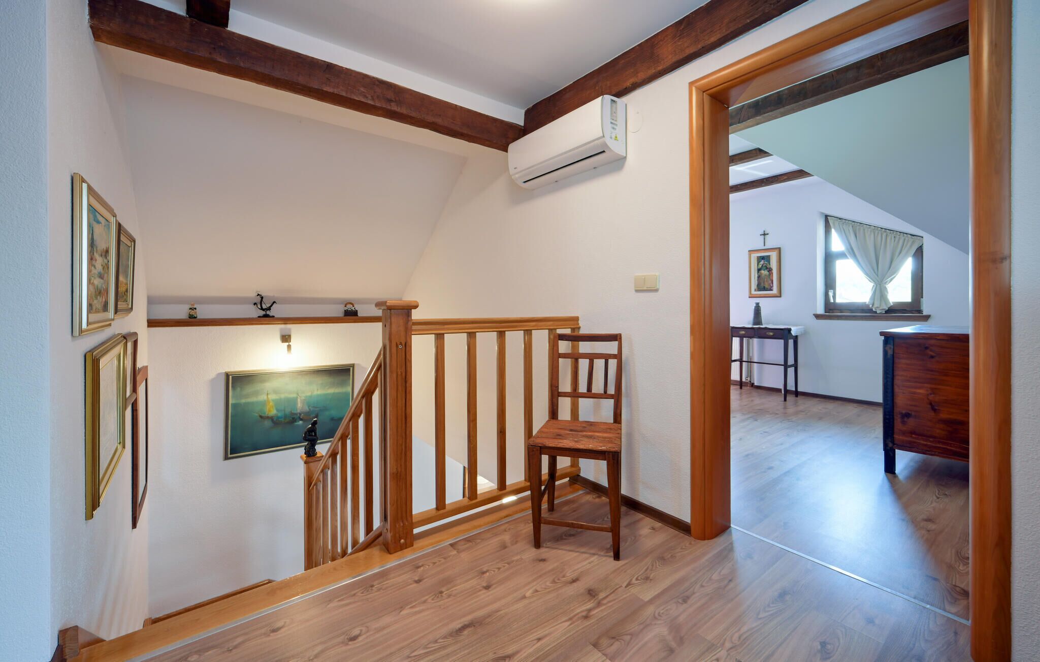 Una scala in legno con una sedia, un quadro e un condizionatore d'aria apposti al muro.